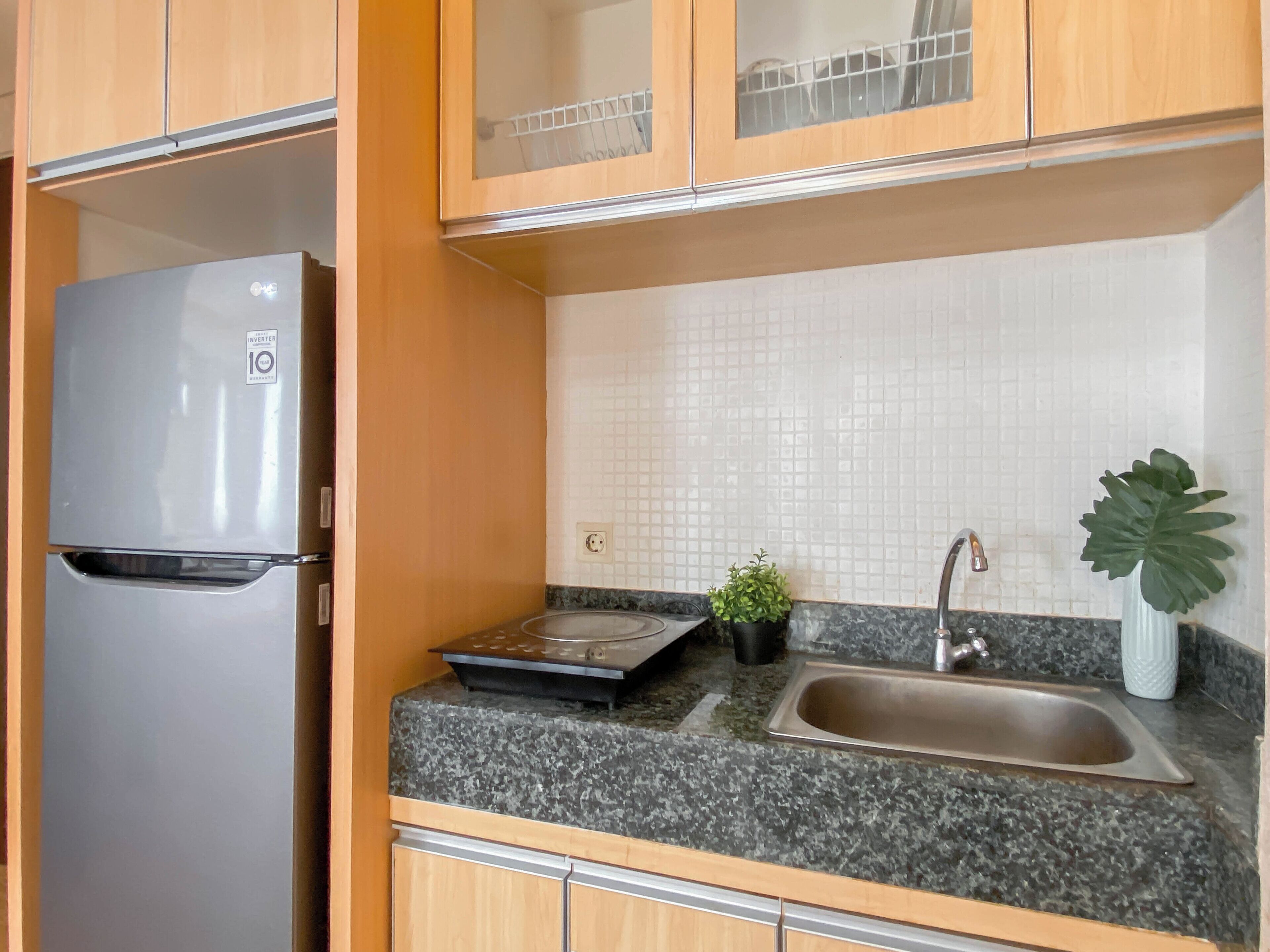 A kitchen with a stainless steel refrigerator, granite countertop, sink, and a small potted plant.