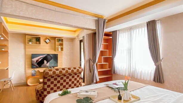 A hotel room with a bed, a TV, a seating area, and a window with curtains. - Good Place And Spacious Studio Transpark Cibubur Apartment (Depok)