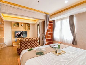 Une chambre d’hôtel comprenant un lit, une télévision, un coin salon et une fenêtre avec des rideaux.