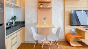 A compact kitchen with a dining area, wooden cabinets, a built-in TV, and a small shelf with plants. - Good Place And Spacious Studio Transpark Cibubur Apartment (Depok)