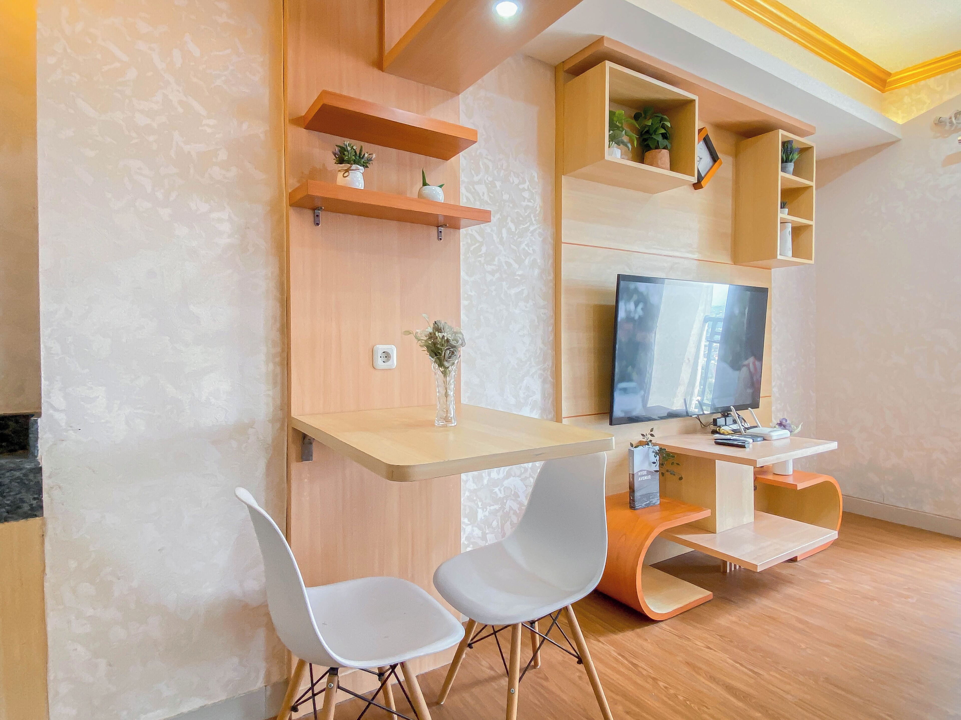 A modern living room with a wooden TV stand, a flat-screen TV, two white chairs, and built-in shelves with plants.