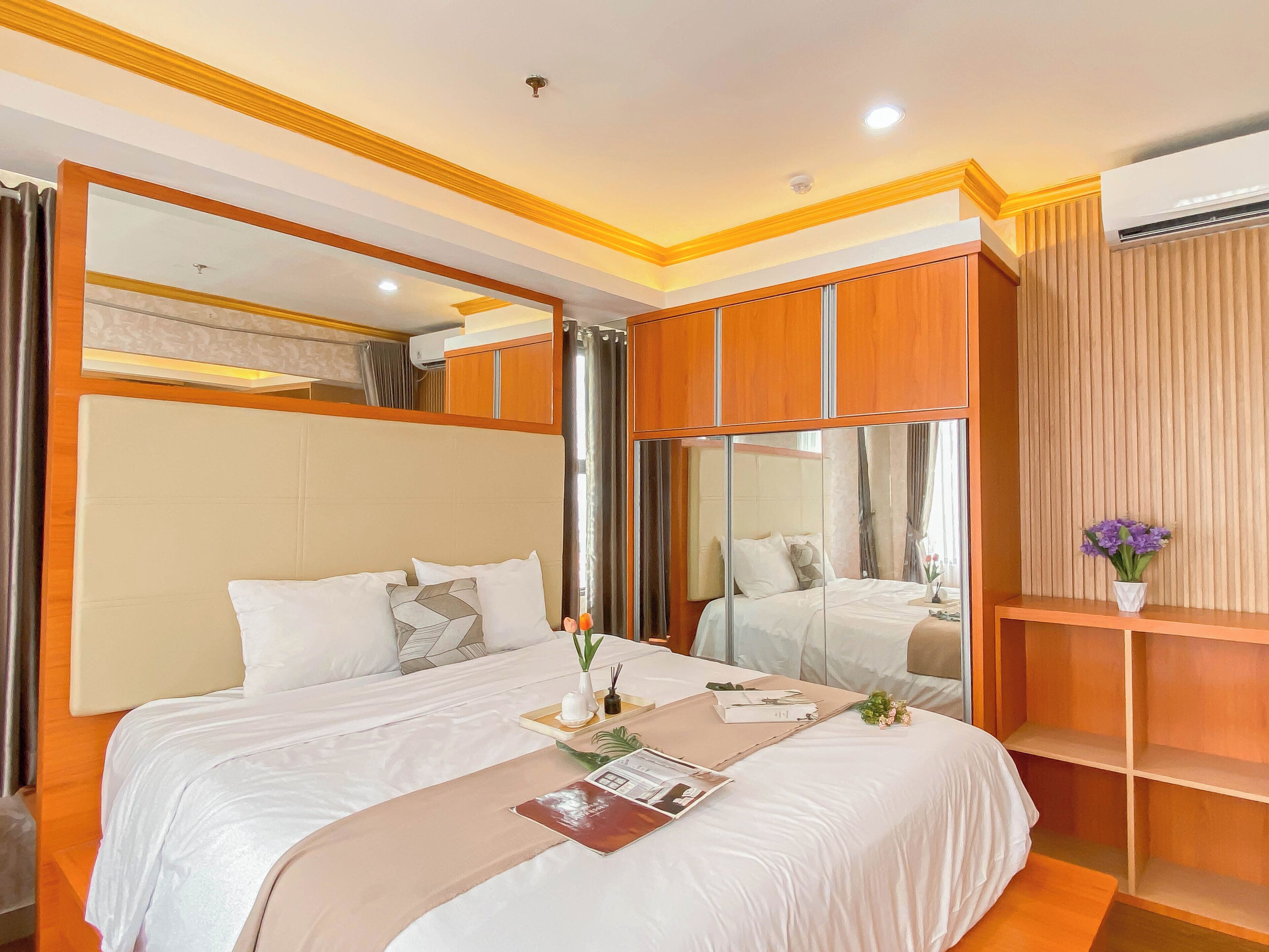 A hotel room with a large bed, a mirror, wooden cabinets, and an air conditioning unit.