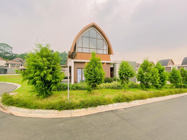 A modern building with a large arched window, surrounded by well-maintained greenery and a curved driveway. - Vimala Hills Villa Gadog Puncak 3Br For 12 Pax (Ciawi)