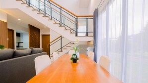 Una sala de estar moderna con una mesa de comedor de madera, un sofá y una escalera que sube a un piso superior.