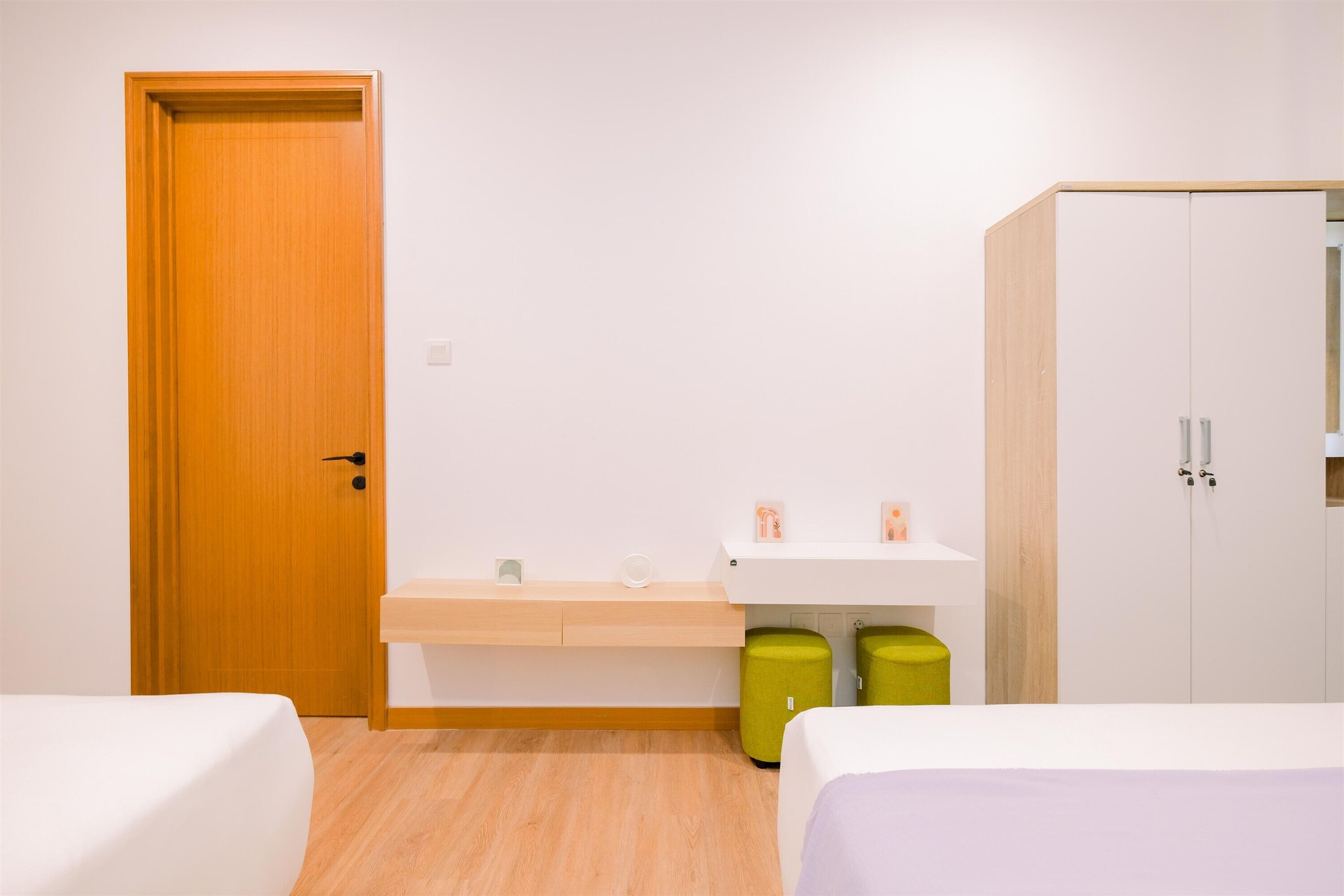 Habitación de hotel con dos camas, una puerta de madera, un lavamanos blanco y un armario.