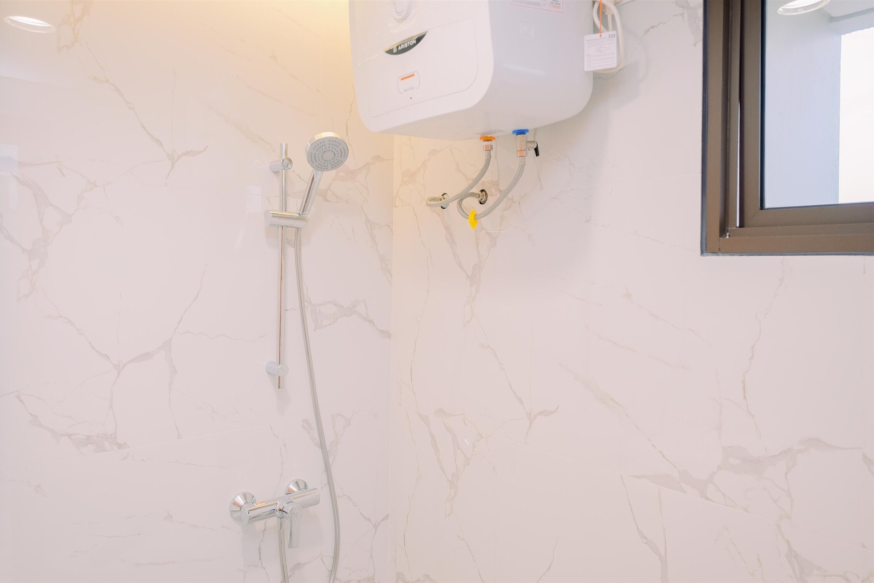 A bathroom with a white marble wall, a showerhead, and a toilet.