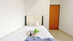 A neatly made bed with a white and beige headboard, a single decorative pillow, and a small plant on a tray beside the bed.