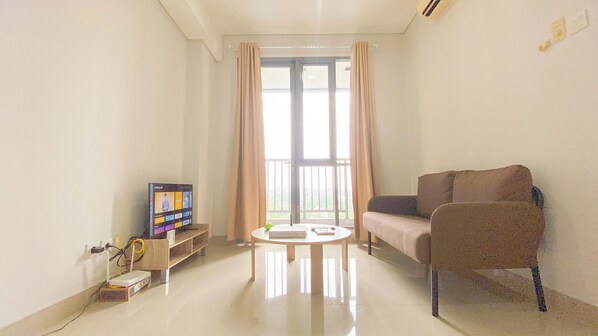 A living room with a flat-screen TV, a sofa, a coffee table, and a window with curtains.