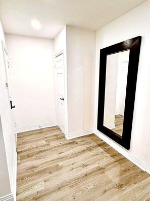 Quarto com piso de madeira, paredes brancas, um espelho grande e uma porta com maçaneta.