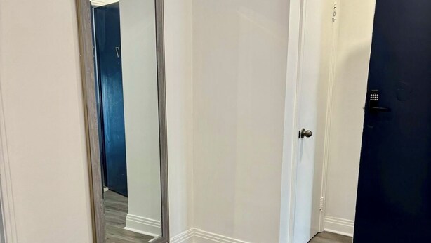 A hallway with a large mirror, a door with a keypad, and a black mat on the floor.