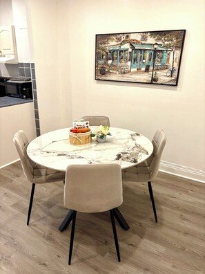 A dining area with a round table, four chairs, a cake, and a vase with flowers.