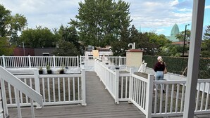 A wooden deck with white railings, potted plants, and a view of a church steeple.