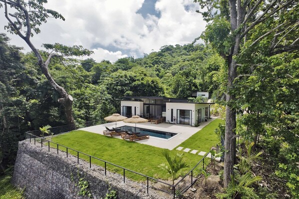 Una casa moderna con piscina, rodeada de abundante vegetación.