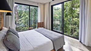 Ein Schlafzimmer mit einem großen Bett, einem Deckenventilator und Blick auf einen üppigen Garten durch große Fenster.