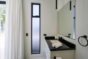 Un baño moderno con un espejo grande, encimera negra y un perchero para toallas.