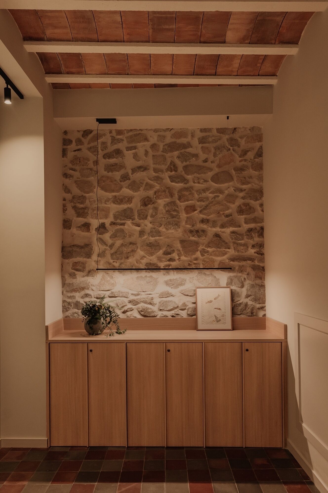 Une pièce avec un mur en pierre, des armoires en bois et un sol carrelé.