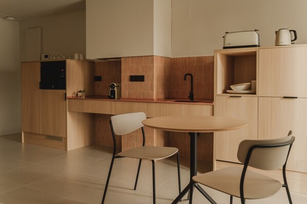 A modern kitchen with wooden cabinetry, a round table, two chairs, a coffee machine, and a kettle on the countertop.