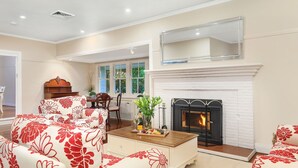 A living room with a fireplace, floral-patterned sofas, a wooden coffee table, and a dining area with a table and chairs. - The Foldgarth – late Victorian era farmhouse (Burradoo)