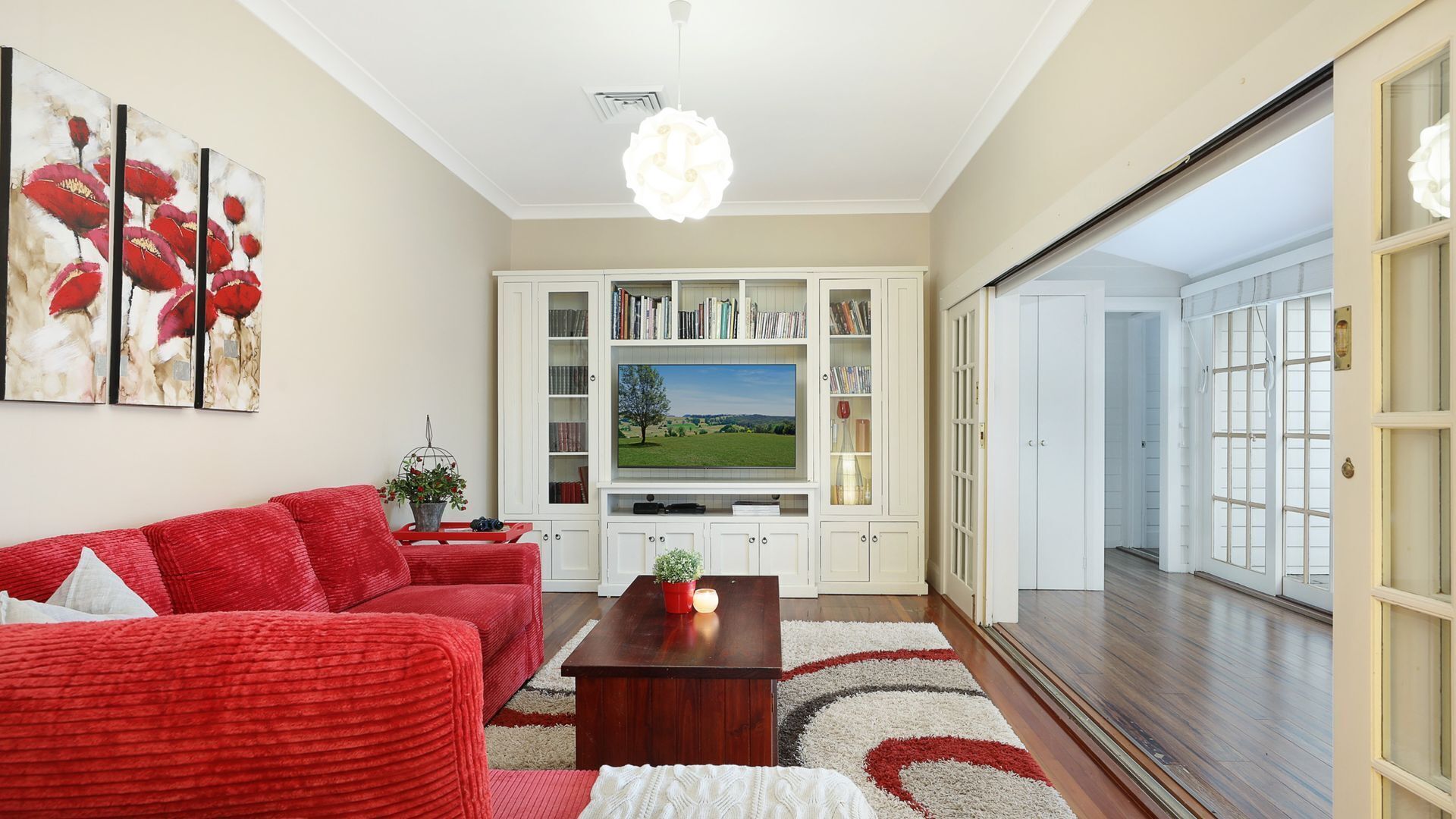 A living room with a red sofa, a wooden coffee table, and a flat-screen TV on a white cabinet.