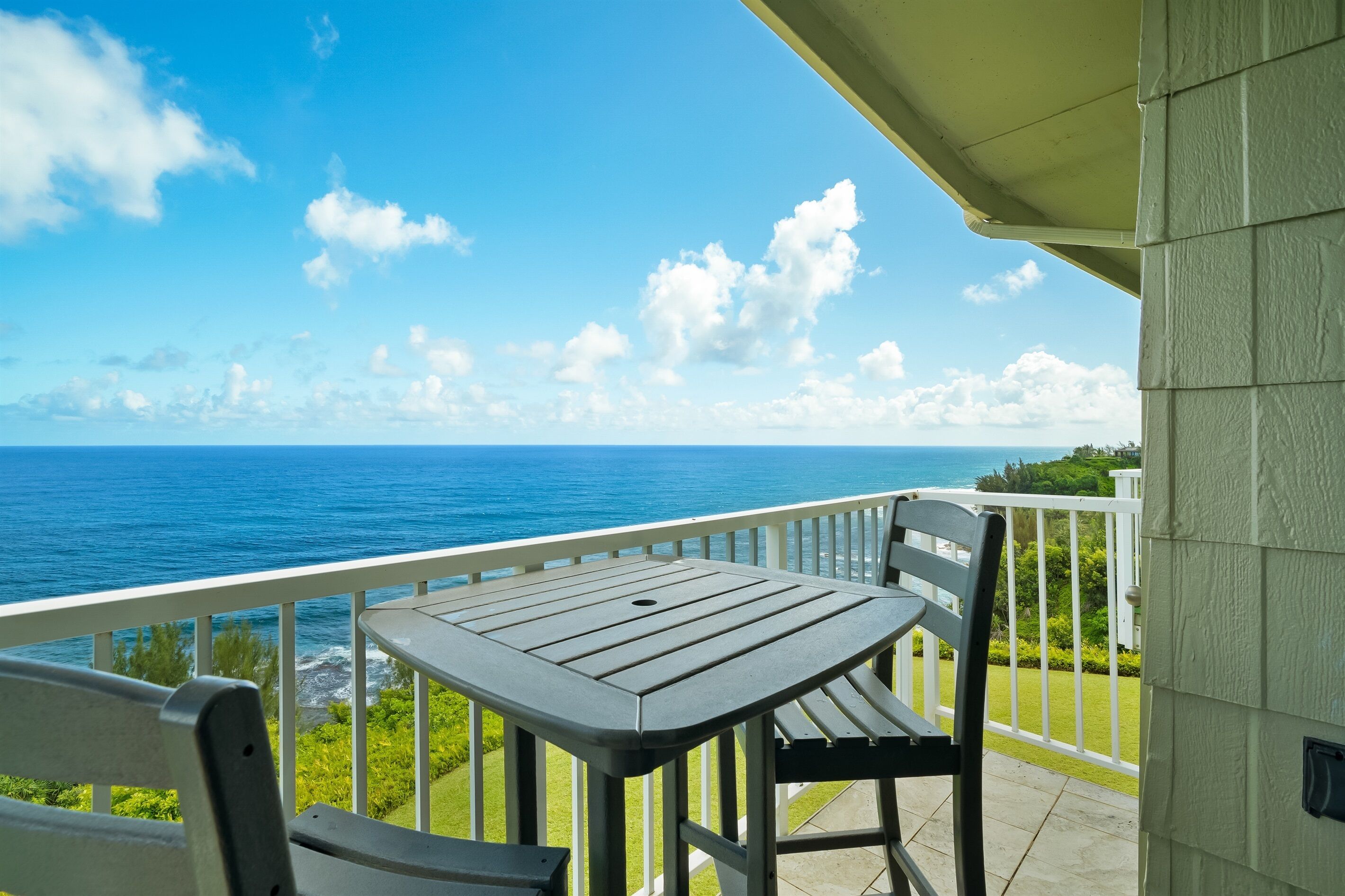 Een balkon met een tafel en stoelen, met uitzicht op een heldere blauwe zee en een groen landschap.
