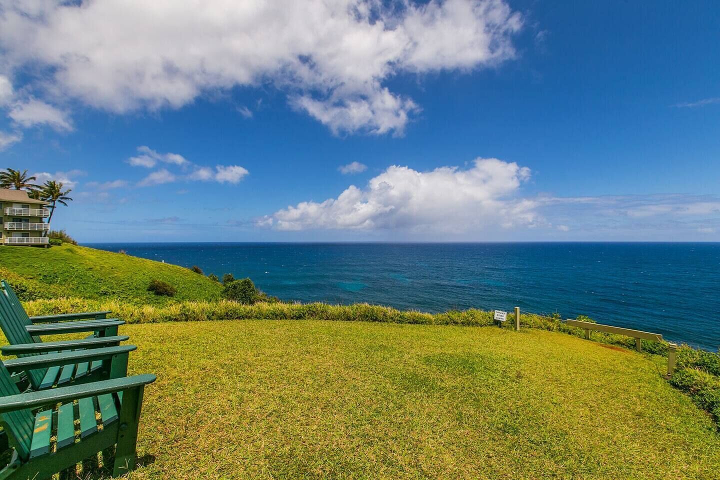 A grassy area with a bench and a building with a balcony overlooking the ocean.