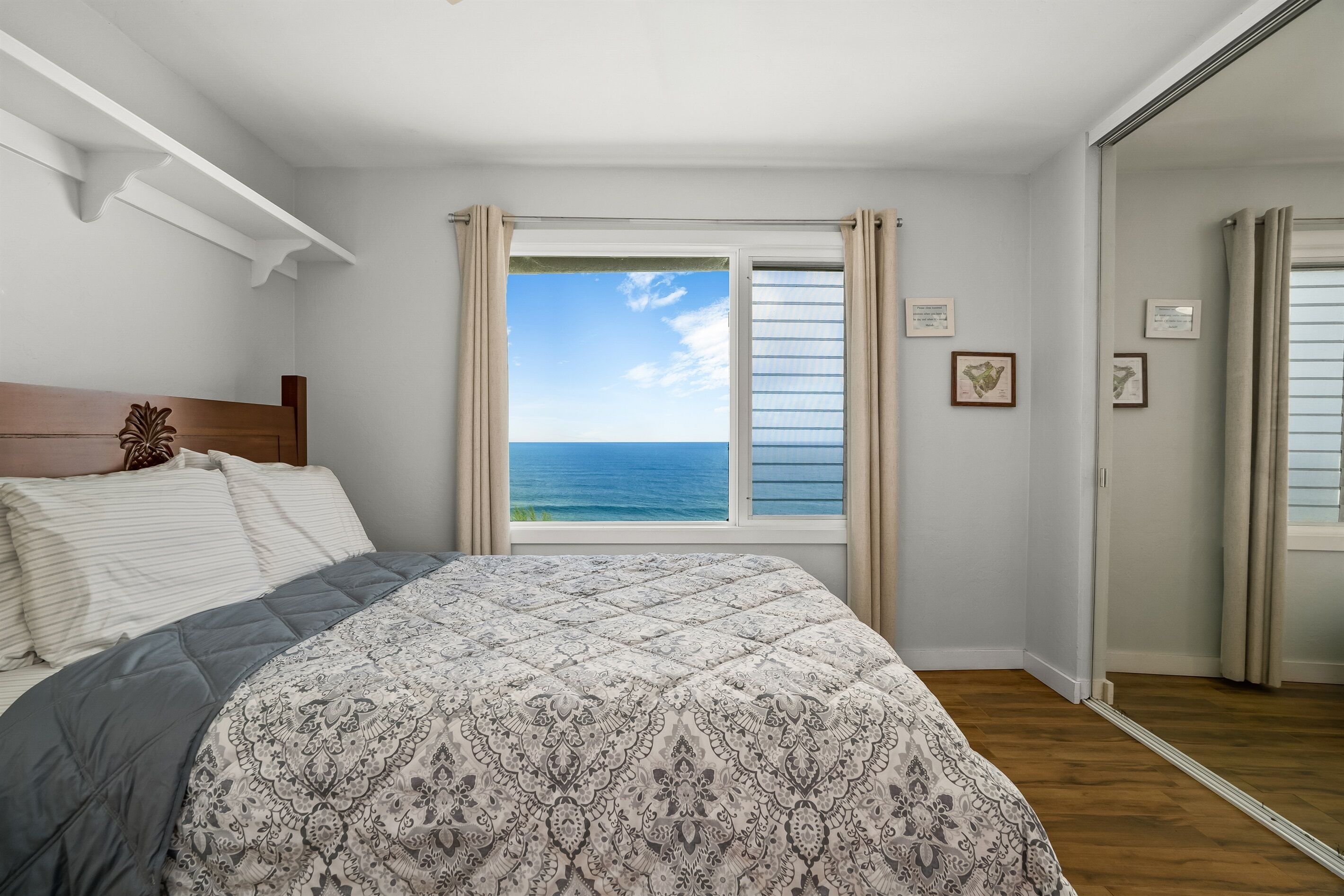 Ein Schlafzimmer mit einem großen Bett, Meerblick durch ein Fenster und einem hölzernen Kopfteil.