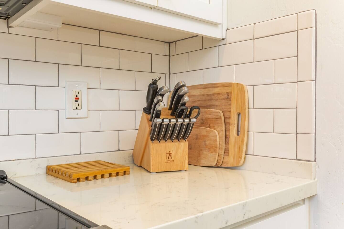 Une cuisine avec des carreaux blancs, une planche à découper en bois, un range-couteaux et un plateau en bois.
