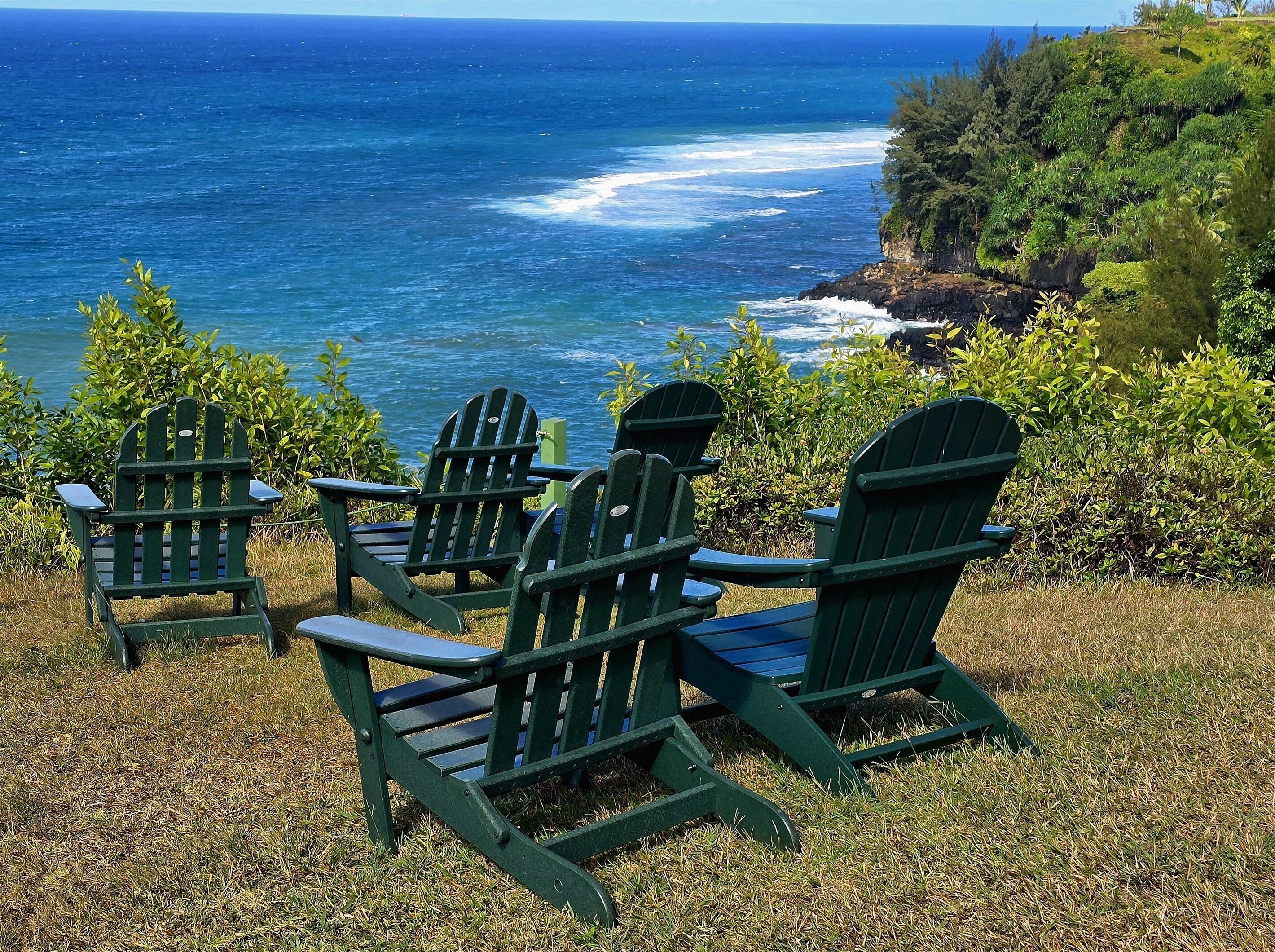 Three green Adirondack chairs facing a view of the ocean.