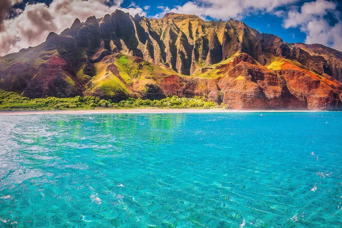 Un paysage côtier avec une eau turquoise cristalline et, en arrière-plan, une chaîne de montagnes accidentée.