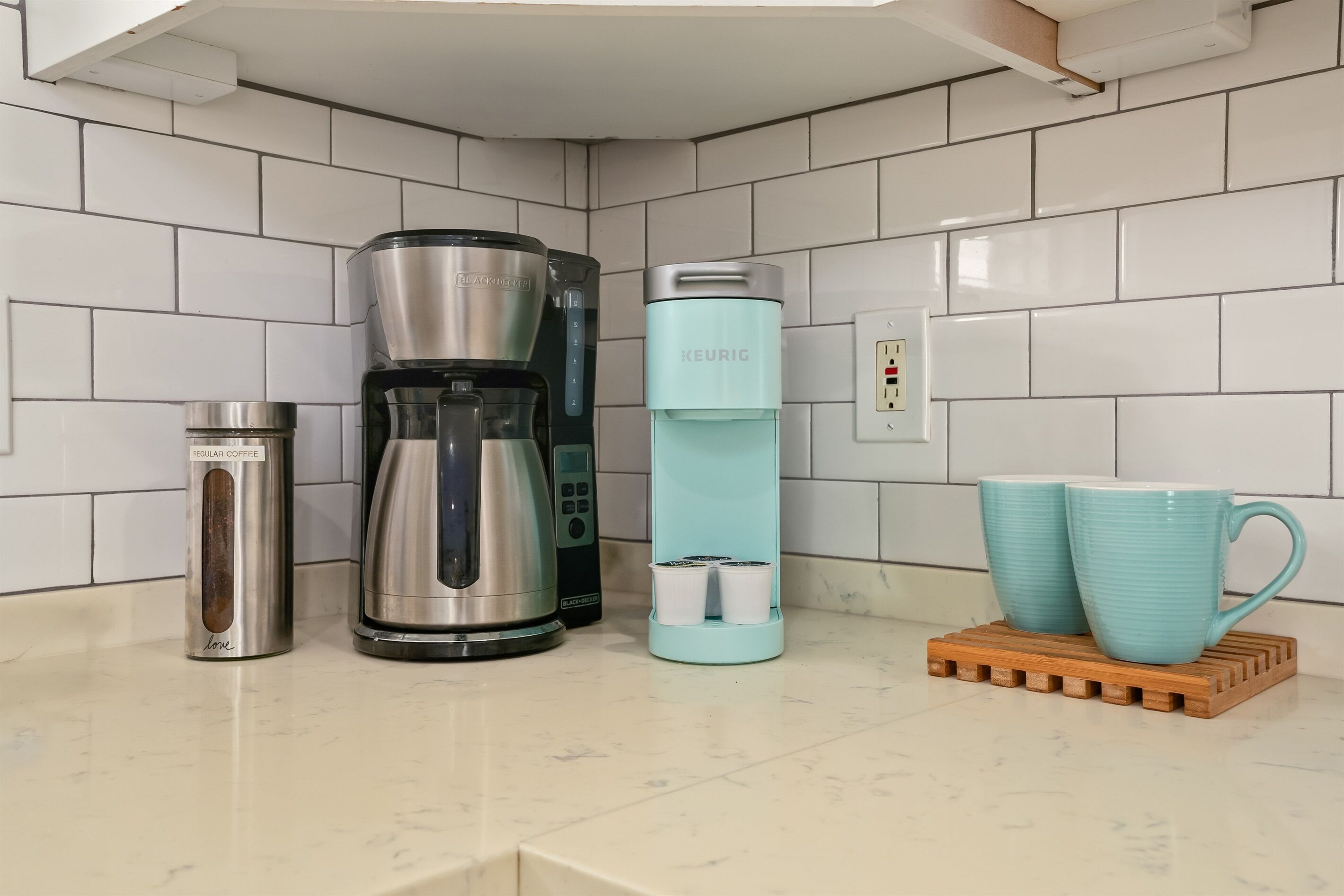 Eine Küchenarbeitsplatte mit einer Kaffeemaschine, einem Wasserspender, einer Thermoskanne und zwei Tassen auf einer Holzwasserrettung.