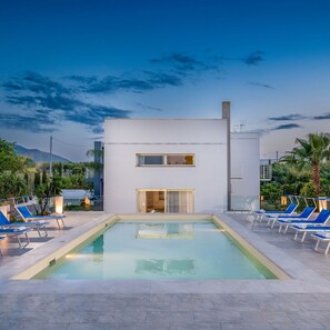 Un edificio moderno con piscina, sillas de descanso y vistas a las montañas.