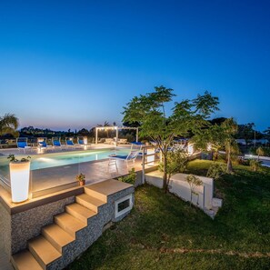 Una piscina con sillones de descanso y una pérgola, rodeada de vegetación y un cielo despejado.