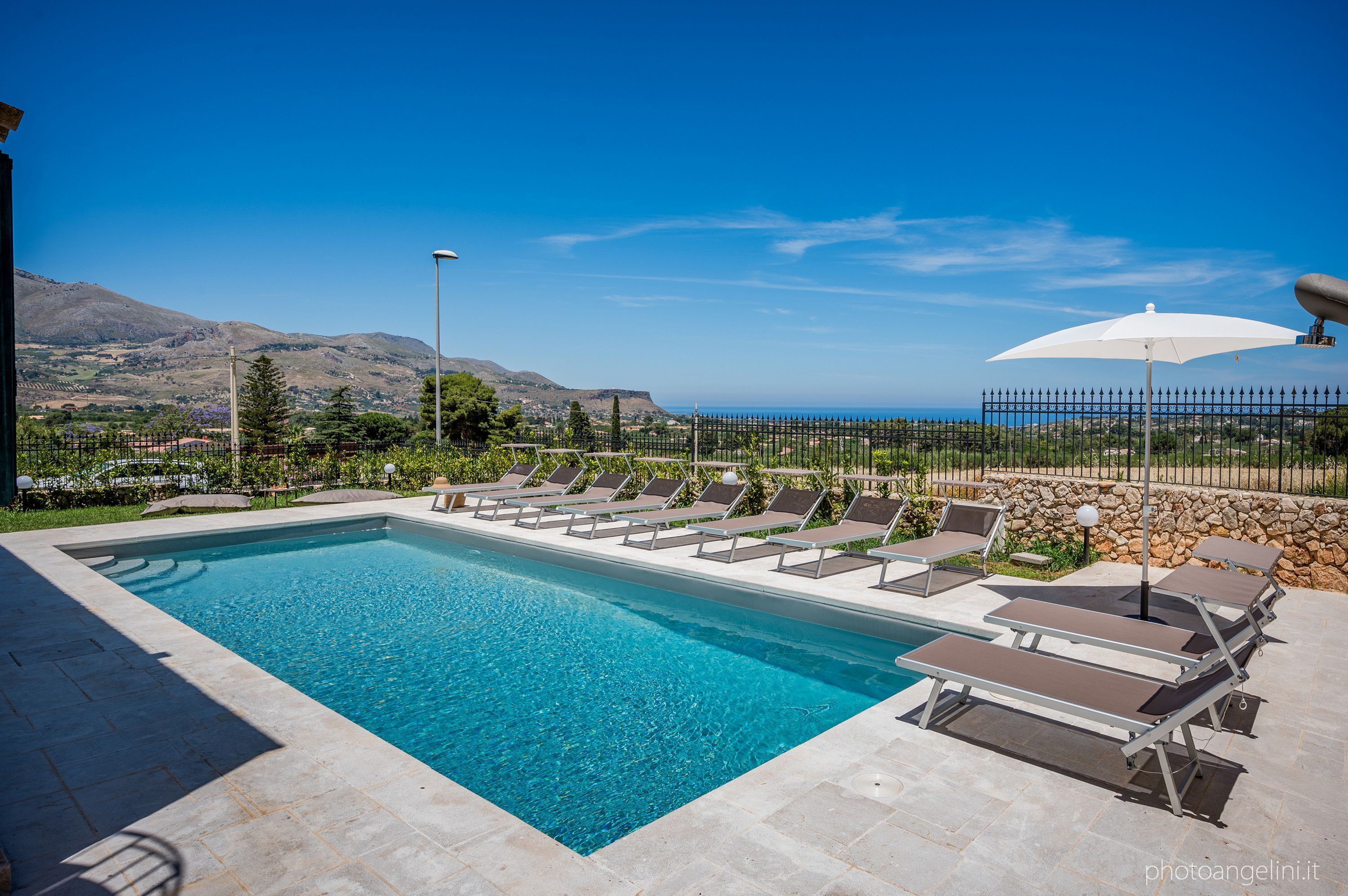 A swimming pool with lounge chairs and a view of the sea and mountains.