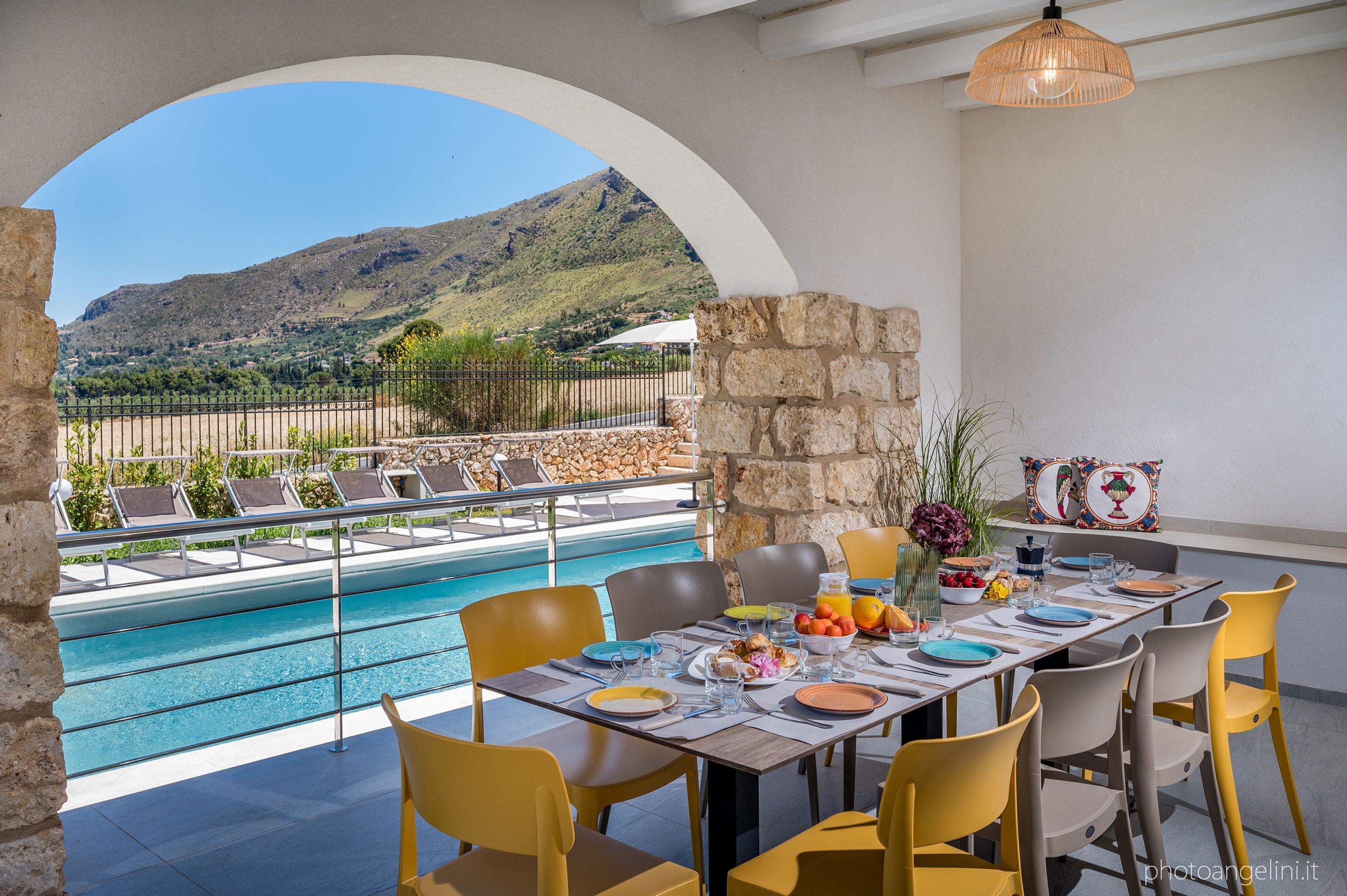An outdoor dining area with a pool view, stone walls, and yellow chairs.