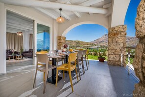 A dining area with a table set for four, a stone wall, and a view of the countryside. - Villa Aglea in Castellammare del Golfo (Castellammare del Golfo)