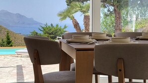 Zona pranzo con tavolo apparecchiato per quattro, ampie finestre con vista su piscina e montagne.
