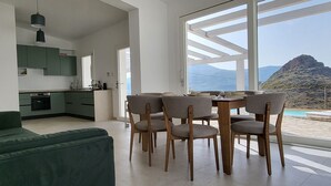 Un soggiorno moderno con divano verde, tavolo da pranzo con sedie, cucina con mobili verdi e un'ampia finestra con vista sulle montagne.
