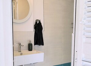 A bathroom with a white sink, a mirror, and a black robe hanging on a rack. - Villa Ballerina Bianca (Castellammare del Golfo)