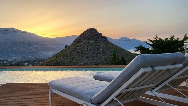 Area piscina con lettini e vista sulle montagne al tramonto.