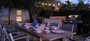 An outdoor dining area with a table set for a meal, surrounded by chairs, and a grill in the background. - Villa Ballerina Bianca (Castellammare del Golfo)