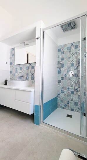 Une salle de bain moderne avec une douche à parois de verre, un meuble-lavabo blanc avec un miroir et des carreaux décoratifs sur les murs.