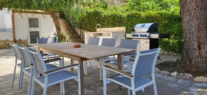 An outdoor patio with a wooden table and white chairs, a grill, and a staircase leading to a covered area. - Villa Ballerina Bianca (Castellammare del Golfo)