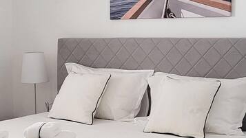 A neatly made bed with white linens and pillows, a grey headboard, and a bedside lamp.