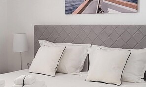 A neatly made bed with white linens and pillows, a grey headboard, and a bedside lamp. - Villa Ballerina Bianca (Castellammare del Golfo)