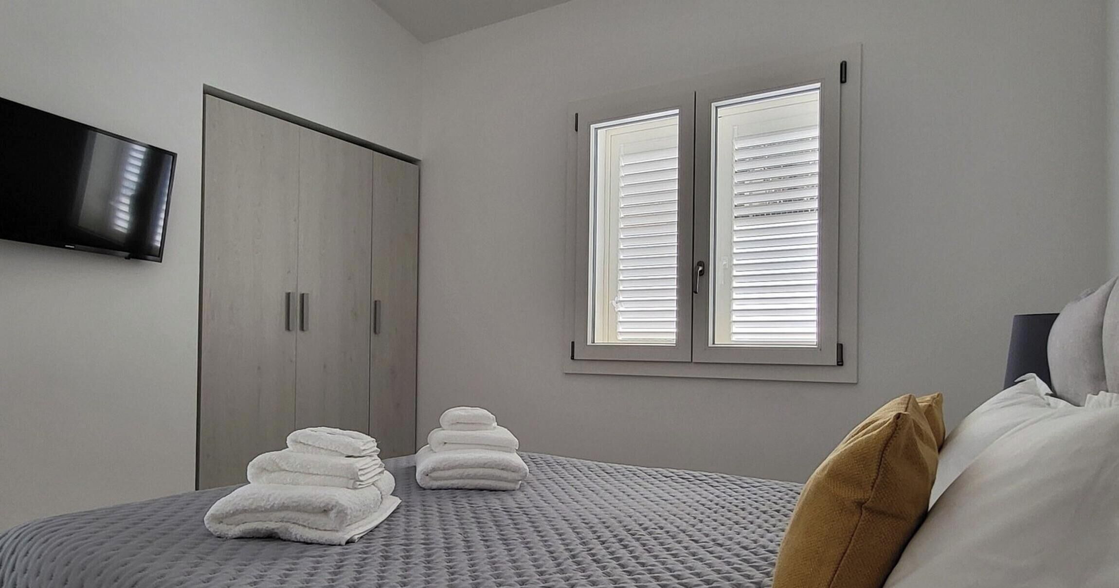 A bedroom with a bed, a wardrobe, a television, and a window with blinds.
