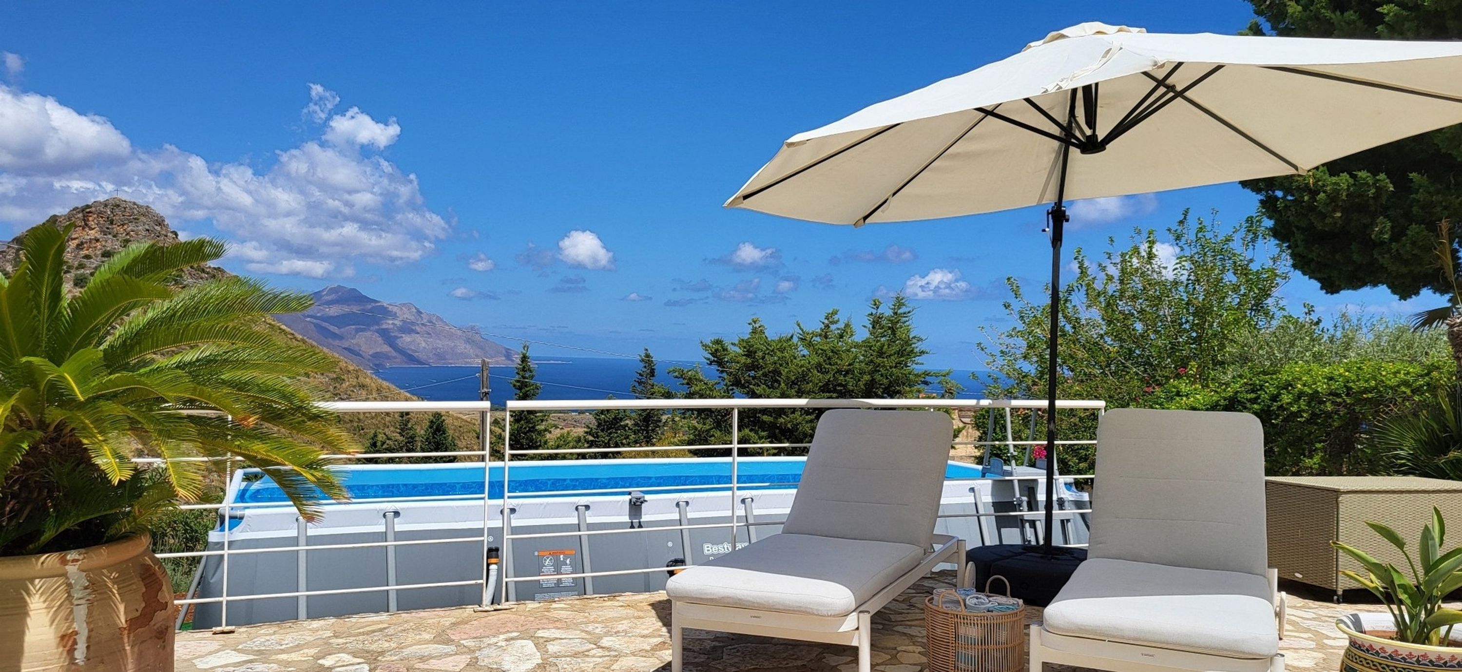 Zona junto a la piscina con sillas de descanso y una sombrilla, con vistas a una piscina y un paisaje montañoso.