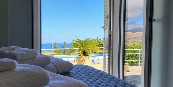 A room with a bed, a window with a view of a pool and palm tree, and a balcony with a view of the sea. - Villa Ballerina Bianca (Castellammare del Golfo)