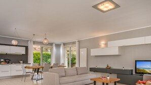 A modern living room with a sofa, coffee table, and a TV. There is a kitchen area with a dining table and chairs. - Villa Jacqueline con Piscina Privata 8 Posti Letto (Castellammare del Golfo)