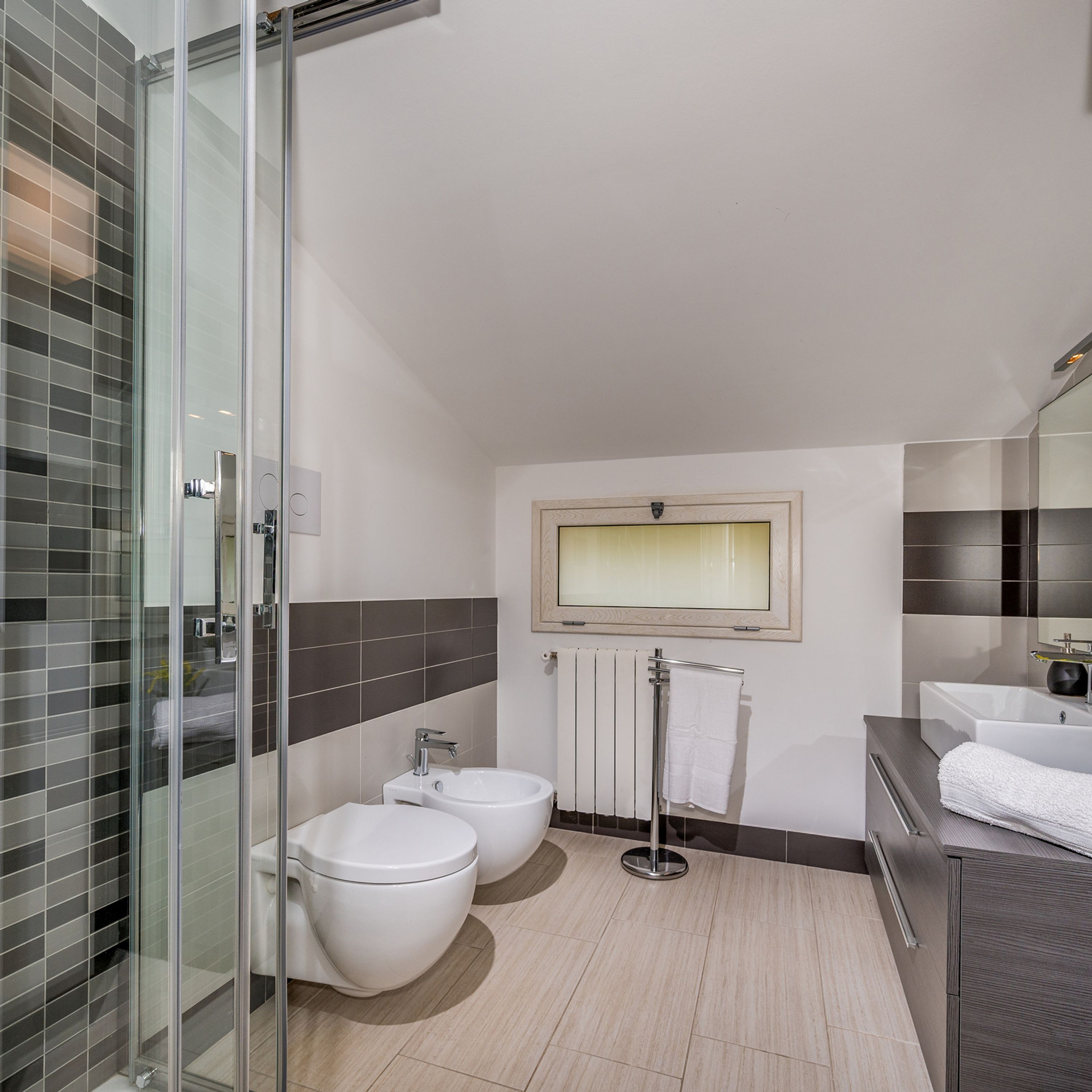 Une salle de bain moderne dotée d’une douche à parois de verre, d’un bidet, de toilettes, d’un porte-serviettes et d’un meuble-lavabo avec un miroir.