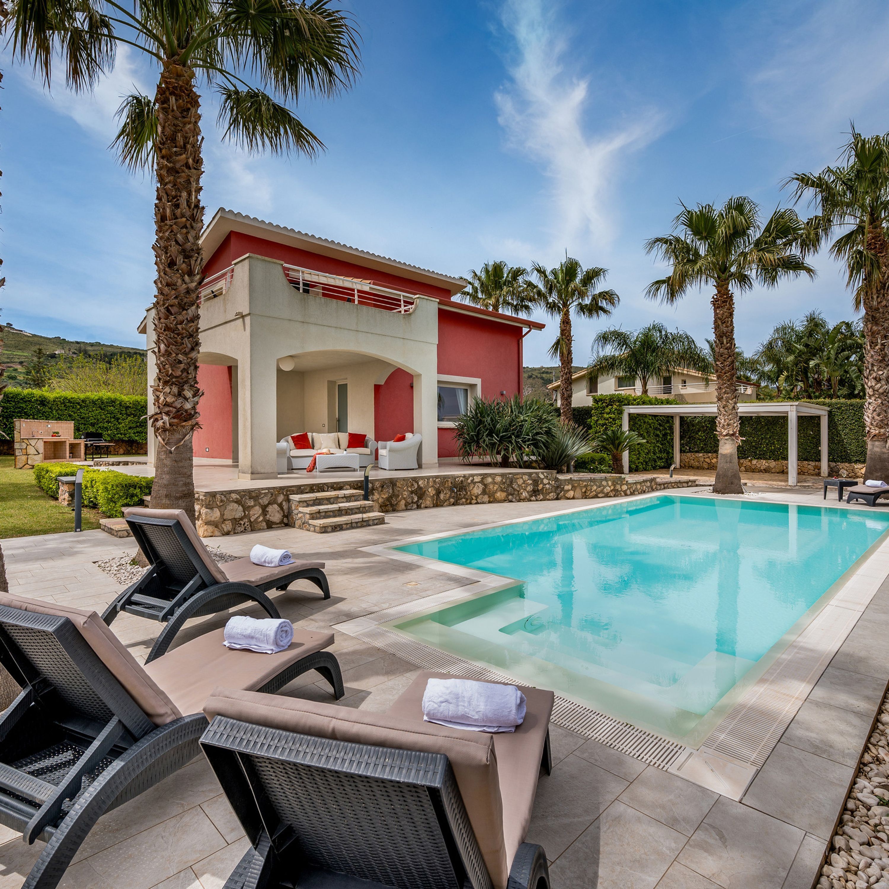 A poolside area with lounge chairs, a pool, and a building with a red facade.